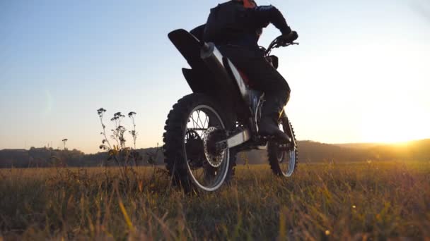 Wiel van motorcross fiets beginnen te draaien en schoppen grond of vuil. Motorfiets start de beweging. Motorrijder rijdt bij zonsondergang. Prachtig landschap op de achtergrond. Langzame beweging Close-up — Stockvideo