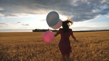 Kırmızı elbiseli mutlu kızın gün batımında elinde balonlarla altın buğday tarlasında koşuşması. Kahverengi saçlı genç kadın arpa çayırında koşarken eğleniyor. Özgürlük kavramı