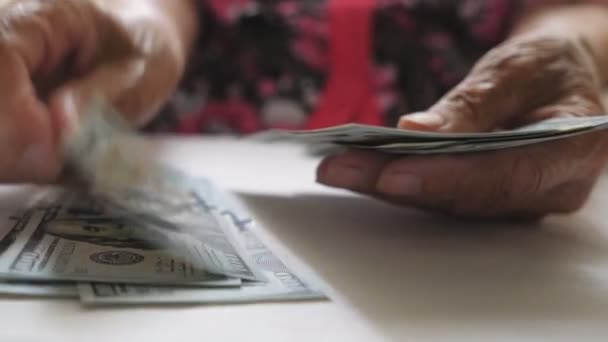 Elderly woman holds cash in arms and counts foreign currency over the table. Close up hands of old grandmother puts one hundred dollar banknotes on the desk. Money concept. Low view Slow motion — Stock Video