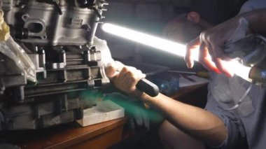 Tamirci garajda veya atölyede otomobil motoru tamir ediyor. Adam işi için karanlıkta parlak el feneri kullanıyor. Tamirci otomatiğe geçti. Yavaş çekim. Yakın çekim.