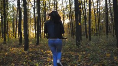Genç bir kadın elinde sarı yapraklarla sonbahar ormanlarında koşar ve onları fırlatır. Canlı yeşillikler yere dökülüyor. Mutlu kız renkli parklarda eğleniyor. Arkaplanda güneş ışığı