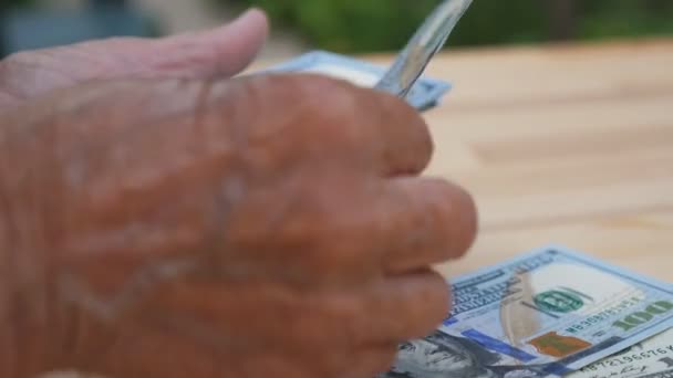 Close up of wrinkled female arms foreign currency and counts cash over the desk. Hands of elderly grandmother puts one hundred dollar banknotes on the table. Money concept. Slow motion — Stock Video