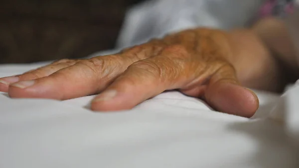 Grandson takes and gently touches hand of his elderly grandmother lying in bed hospital. Young man comforts wrinkled arm of sick mature woman in medical clinic. Concept of care and love. Slow motion.