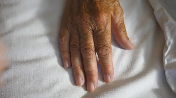 孙女抬起并轻轻触摸躺在病床上的生病的成熟奶奶皱巴巴的胳膊 女孩在诊所安慰她祖母的手 关心和爱的概念 顶部视图 — 图库照片