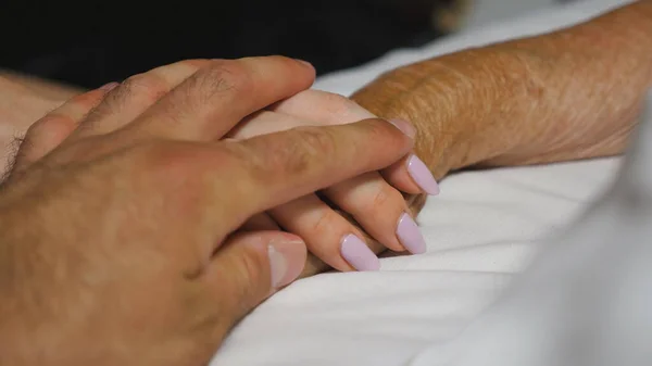 孙女和孙子轻轻地摸着躺在病床上的奶奶的手 在诊所里 年轻男女舒适地挽着生病的祖母的皱纹的胳膊 关心和爱的概念 靠近点 — 图库照片#