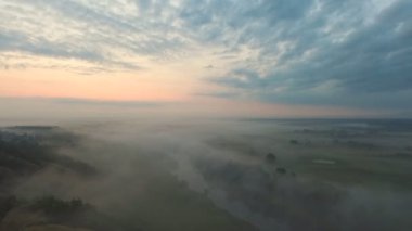 Sabahın erken saatlerinde güzel kırsal çevrenin hava görüntüsü. Şafakta sisli vadi ve ufukta inanılmaz manzara. Gün doğumunda sisle geniş çayırlarda uçmak. Yavaş çekim