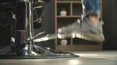 Erkek ayak sandalyede pedala basar ve saç kesiminden önce kaldırır. Koltuğun yüksekliğini ayarlayan berber. Berber dükkanında çalışmaya hazırlanan adam. Arka plan bulanık. Yavaş çekim Yan Görünümü Kapat