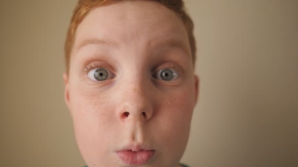 Mały rudowłosy chłopiec spoglądający w kamerę z wyrazem wow wewnątrz. Portret rudego dziecka z piegami ukazujący zaskoczenie i zdumienie. Zamknij zszokowaną męską twarz małego dziecka w środku. Zwolniony ruch — Wideo stockowe