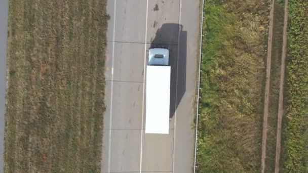 Flygfoto av lastbil med vit lastvagn som kör på tom väg och transporterar gods. Flyger över en lastbil som kör genom landsvägen. Logistiskt koncept. Ovanifrån — Stockvideo