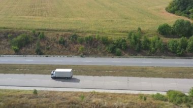 Kargo karavanıyla birlikte yolda giderken ve malları taşırken çekilen hava görüntüsü. Çevrede doğa manzarası olan taşra otoyolunda nakliye kamyonunun üzerinde uçmak. Yan görünüm