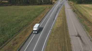 Boş yolda giden ve malları taşıyan kargo karavanı olan bir kamyonun hava görüntüsü. Teslimat kamyonunun üzerinden uçup kırsal kesimden geçen bir otoban. Çevrede güzel kırsal çevre