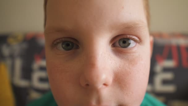 Portret van kleine wanhopige roodharige jongen met sproeten die binnen in de camera kijkt. Sluit een mannelijk gezicht van een treurig kind. Wanhopig roodharig kind zittend op de bank. Teleurgestelde blik van kleine man — Stockvideo