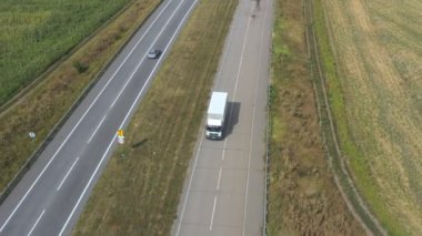 Boş yolda giden ve malları taşıyan kargo karavanı olan bir kamyonun hava görüntüsü. Taşra otobanı boyunca giden teslimat kamyonunun üzerinde uçuyor. Çevrede güzel bir kırsal bölge var. Yavaş çekim