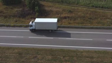 Kargo karavanıyla birlikte boş düz yolda giden bir kamyonun görüntüsü. Beyaz kamyonun üzerinden uçup kırsal alandan geçen bir otoban. Lojistik ve teslimat kavramı. Yan görünüm Yavaş çekim