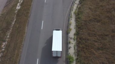 Varış yerine giden yolda beyaz kargo römorklu bir kamyonun hava görüntüsü. Kırsal yolda ilerleyen kamyonun üzerinde uçuyor. Lojistik veya teslimat kavramı. Üst Görünüm Yavaş Çekim