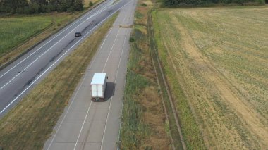 Düz yolda giden ve malları taşıyan kargo karavanı olan kamyonun hava görüntüsü. Kameralar taşra otobanından geçen teslimat kamyonunu izliyor. Kırsal kesimde trafiğin üzerinde uçmak.