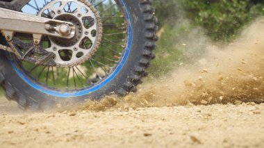 Güçlü off-road motorsiklet tekerlerini kapatın. Dönüyor ve kuru zemini tekmeliyor. Profesyonel motokros yarışçısı yarışa ya da eğitime başlıyor. Aktif yaşam tarzı konsepti. Yan görünüm Yavaş çekim.
