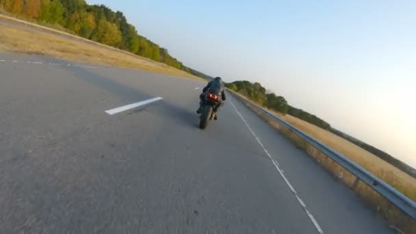 高速道路で現代のスポーツバイクに乗ってバイカーの周りを移動するカメラ。オートバイ愛好家は日没時に田舎道でバイクレースをする。旅行中に自転車を運転する男。自由と冒険の概念 — ストック動画