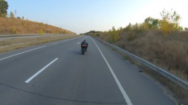 Sonbahar otobanında motosiklet süren motosikletliyi takip edin. Motosikletli, kır yolunda motosikletiyle yarışıyor. Yolculuk sırasında bisiklete binen adam. Özgürlük ve macera kavramı. Hava görüntüsü