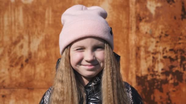 Hermoso niño pequeño con el pelo largo y rubio entrecerrando los ojos y mirando a la cámara al aire libre. Acércate a las emociones de la niña sonriente con expresión alegre en su cara. Retrato de una niña feliz afuera — Vídeo de stock