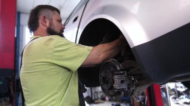 Sarı tişörtlü yetenekli otomotiv teknisyeni araç tamiri, araç süspansiyonu üzerinde çalışmak, profesyonel garaj ortamında uzmanlık ve kendini adamışlık göstermek için araçlar kullanıyor..