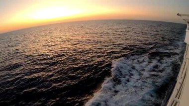 Üç çerçeveli okyanus manzarası, suda yansıyan güzel günbatımı renklerini gösteriyor, bir teknenin arkasında hafif dalgalar, dingin atmosferi arttırıyor.