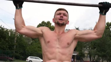 Sporcu güçlü bir barfiks çekiş sahnesine girer, kas gücünü ve odaklanmayı vurgular, canlı bir arka plan üzerine kurulur, fitness ve eğitime olan bağlılığını gösterir.