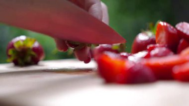 Eller ahşap kesim tahtasında taze çilekleri ustalıkla dilimliyor, canlı renkler ve dokular sergiliyor, yemek hazırlıklarında aşçılık hazırlığı ve detaylara dikkat gösteriliyor.