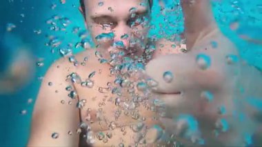 Sualtı sahnesinde, kabarcıklar arasında coşkuyla baş parmak gösteren bir adam parlak mavi bir su ortamında neşeli bir atmosferi vurguluyor.