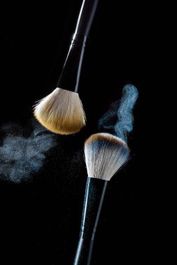 Siyah bir arka plan üzerinde hareket halinde mavi makyaj gölgeleri ile makyaj için iki fırça