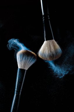 Siyah bir arka plan üzerinde hareket halinde mavi makyaj gölgeleri ile makyaj için iki fırça