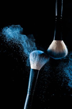 Two brushes for makeup with blue make-up shadows in motion on a black background clipart