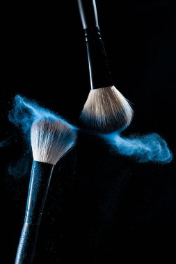 Two brushes for makeup with blue make-up shadows in motion on a black background clipart