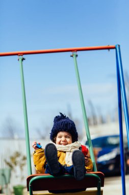 mutlu çocuk ceket şapka ve atkı bir salıncak üzerinde sürme