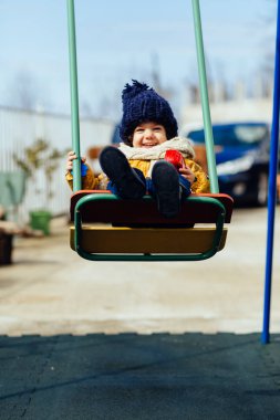 mutlu çocuk ceket şapka ve atkı bir salıncak üzerinde sürme