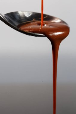 Erimiş sütlü kahverengi çikolata bir kaşık tan dökülen, beyaz yakın izole