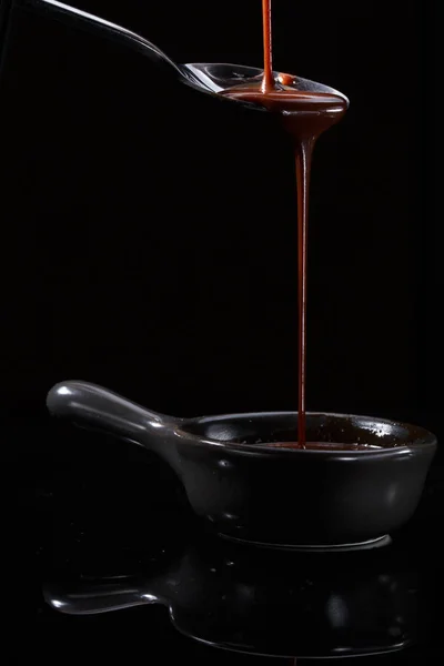 Melted milky brown chocolate pouring from a spoon, isolated on black — Stock Photo, Image
