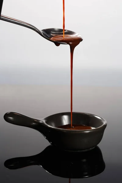 Melted milky brown chocolate pouring from a spoon, isolated on white — Stock Photo, Image