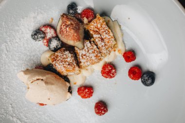 Kuru üzüm, taze çilek ve kuru üzüm ve elma ile strudel dondurma Dilimleri ile Strudel, taze çilek ile beyaz bir tabak üzerine pudra şekeri serpin