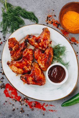 gri arka plan üst görünümünde beyaz plaka üzerinde domates soslu ızgara tavuk kanatları