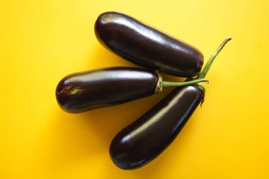 Sarı bir arka plan, yatay üzerinde üç taze siyah organik patlıcan üzerinde üstten görünüm