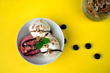 Vanila ve çilek dondurmalı çikolata ve nane ile fındık ve yaban mersini beyaz kase sarı arka camına. Üç kaşık toz. Genel gider atış.