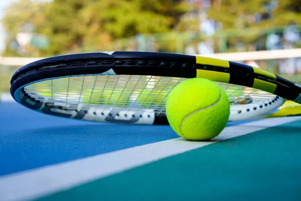 Tennis ball and racket on white Court line on hard modern blue court with Net balls trees in the background. Summer autumn time