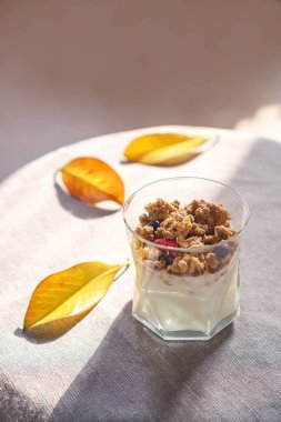 Yunan yoğurt granola ile çilek cam ve sarı yaprakları kurutulur. Rustik tarzı bezle gri arka plan. Üstten görünüm kopya alanı. Sağlıklı sonbahar kahvaltı yaşam tarzı bloglama için fikirler