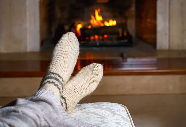 Feet in woollen socks and knitted plaid in front of the fireplace. Close up on feet. Cozy relaxed magical atmosphere home interior. Christmas New Year holidays winter concept. Horizontal