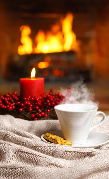 Noel dekorasyon şömine önünde rahat örme şal üzerinde buhar ve çerez meyveleri kırmızı mum ile sıcak içecek fincan. Yılbaşı yeni yıl kavramı. Rahat rahat büyülü atmosferi.
