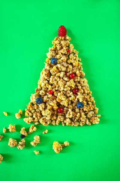 Christmas healthy lifestyle layout granola or muesli in shape of Christmas tree with balls of berries and raspberry on top on green background. New Year concept for diet healthy breakfast. Flat lay — Stock Photo, Image