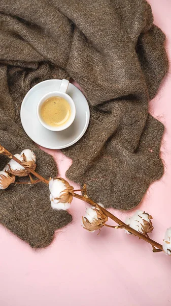 Russian woolen shawl with cup of coffee and cotton branch on pink pastel color background. Romantic winter concept for blogger. Top view, copy space