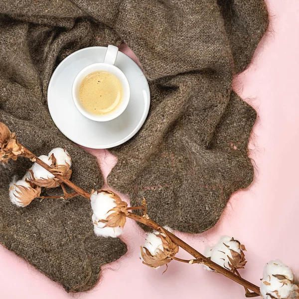 Flat lay Russian woolen shawl with cup of coffee and cotton branch on pink pastel color background. Romantic winter concept for blogger. Top view, copy space