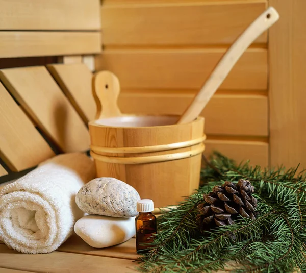 Spa, sauna and wellness setting with water bucket, oil essence, cones, Christmas tree branches, white towel on wooden background. winter wellness concept relax and treatment therapy. Selective focus